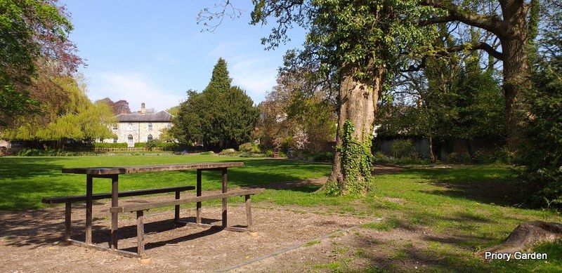 A picnic table in the foreground with a lawn and trees leading back to a building