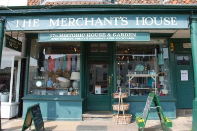 a photo of a shop.  Painted green with large display windows.  A sign reads The Merchant's House