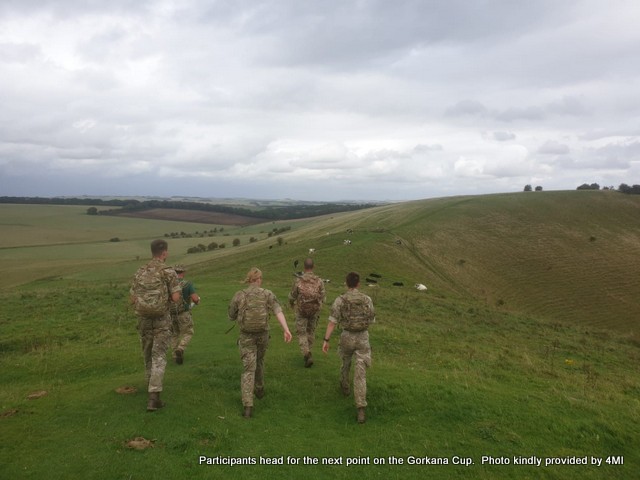 men and women in army uniform walk away from the camera along a hilltop