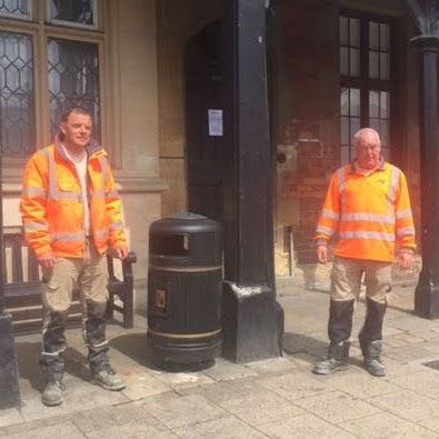 two men in hi viz jackets standing beside a litter bin on a pavement