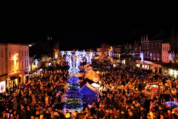 a street at night. There are crowds of people with market stalls and coloured lights above