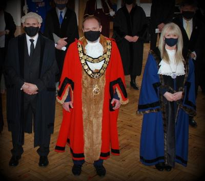 Two men and one woman stand facing the camera.   They wear robes and chains of office