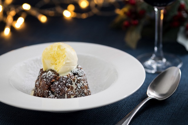 A white bowl contains a dark Christmas pudding topped with a ball of ic-cream