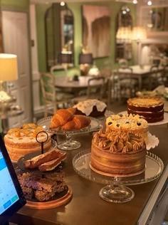 assorted cakes sit on a counter.  There are cafe chairs and tables behind