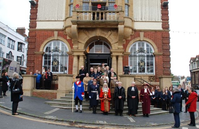 a group of people in ceremonial dress stand on steps in front of a large ornate building.  Some salute