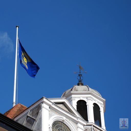 a blue sky.  there is a flag flying from a pole on the roof of a building. An ornate cupola is to the right hand side