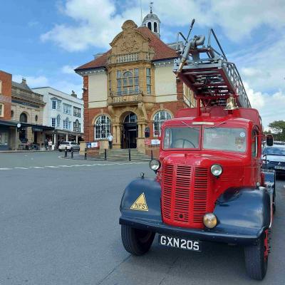 an old fire engine painted red with a brass bell and a ladder on the roof.  Behind it is an elaborate building