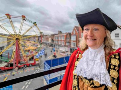 A woman wearing red mayoral robes with a fairground in the background