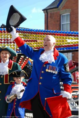 a woman in town crier robes raises her tricorn hat