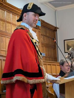 A man in a red gown and chain of office stands at a lectern